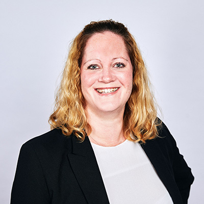 A headshot of a lady with a blonde bob, wearing a black blazer and white top smiling at the camera.