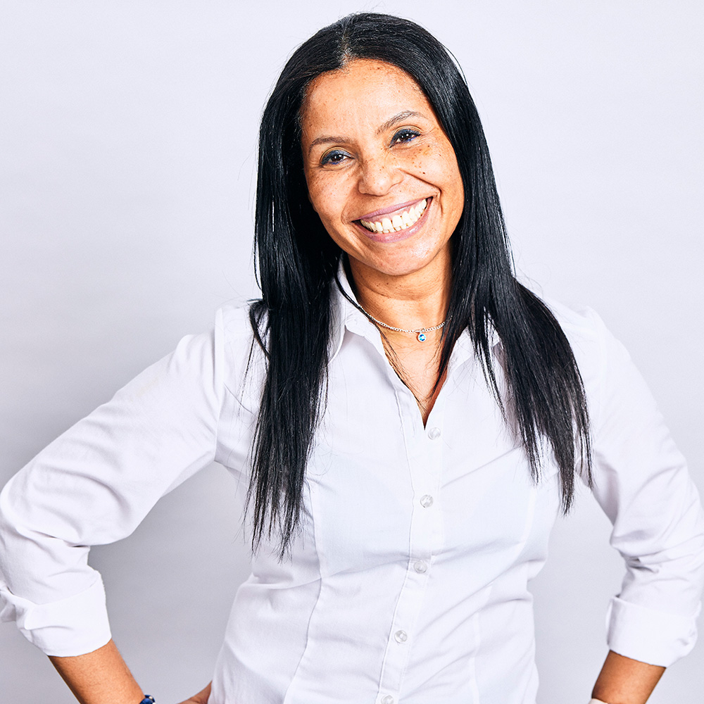 A headshot of a lady with long, black hair in a white shirt, smiling at the camera.