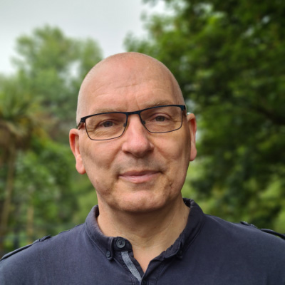 A headshot of a bald man, wearing glasses and a polo shirt, smiling at the camera.