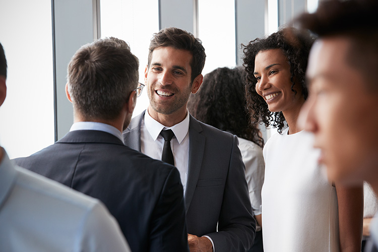 Man and lady in business attire looking at a man whose back is facing us and smiling.